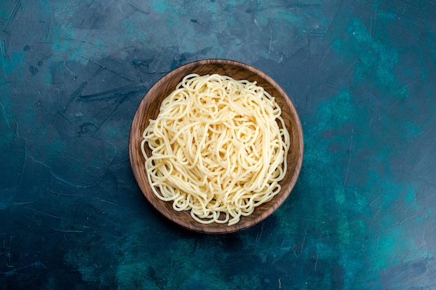 Vue de dessus des pâtes italiennes cuites à l'intérieur de la plaque en bois ronde sur fond bleu pâtes alimentaires dîner pâte viande