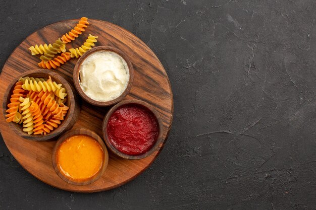 Vue de dessus des pâtes italiennes cuites pâtes en spirale inhabituelles avec des assaisonnements sur un bureau sombre repas de pâtes dîner plat de cuisson des aliments