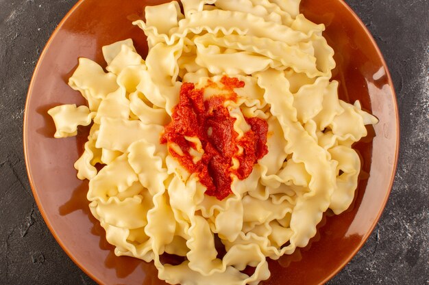 Une vue de dessus des pâtes italiennes cuites avec sauce tomate à l'intérieur de la plaque sur la table grise repas alimentaire pâtes italiennes