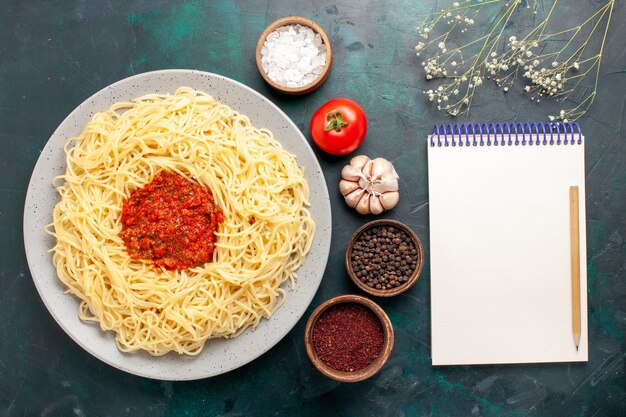 Vue de dessus des pâtes italiennes cuites avec sauce tomate à la viande hachée et assaisonnements sur bureau bleu