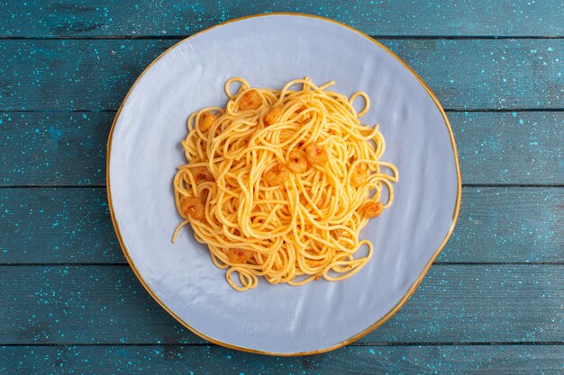 Vue de dessus des pâtes italiennes cuites savoureuses à l'intérieur de la plaque bleue sur la surface rustique en bois bleu