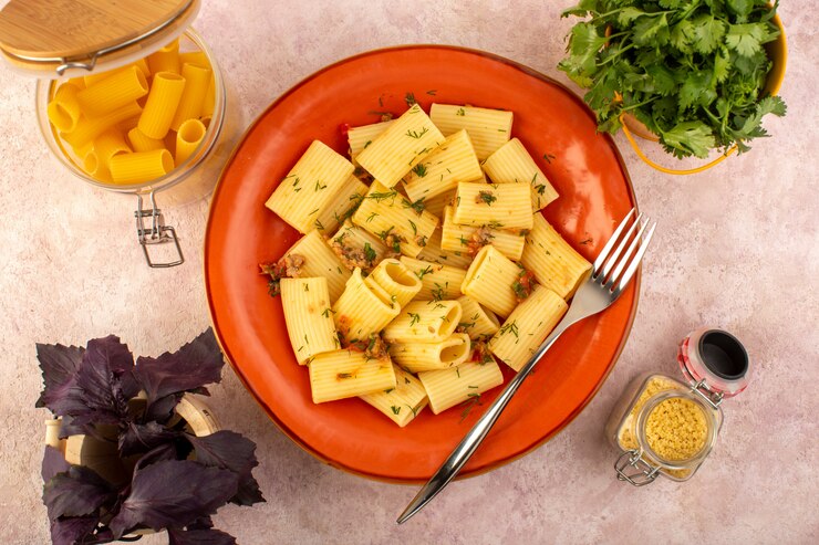 Photo gratuit une vue de dessus pâtes italiennes cuites savoureuses salées à l'intérieur de la plaque orange ronde avec des fleurs et des pâtes crues sur un bureau rose