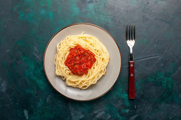 Vue de dessus des pâtes italiennes cuites avec de la viande hachée et de la sauce tomate sur le bureau bleu foncé