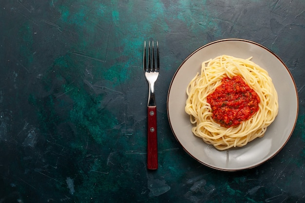 Vue de dessus pâtes italiennes cuites avec viande hachée et sauce tomate sur la surface bleu foncé