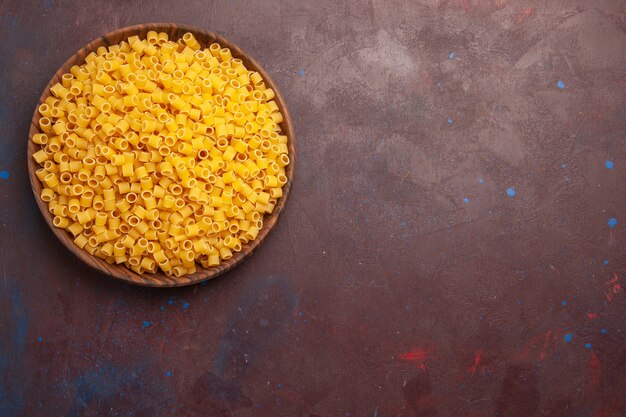 Vue de dessus des pâtes italiennes jaunes crues peu formées sur un bureau sombre pâte de repas crue de nourriture de pâtes