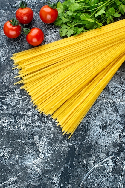 Vue de dessus des pâtes longues crues avec des verts et des tomates sur fond gris couleur pâte à pâtes cuisine cuisine cuisine cuisine cuisine