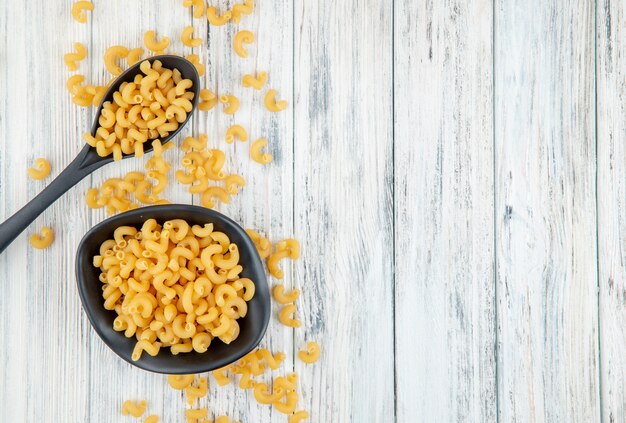 Vue de dessus des pâtes macaroni au coude sur la gauche avec copie espace sur fond de bois blanc