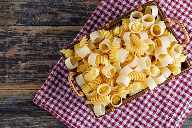 Photo gratuite vue de dessus des pâtes macaroni dans un panier sur un tissu de pique-nique et un fond en bois. espace horizontal pour le texte