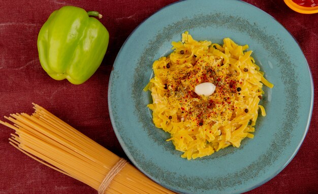 Vue de dessus des pâtes macaroni en plaque avec du poivre et des vermicelles sur la surface du tissu bordo