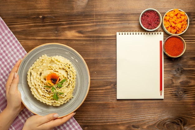 Photo gratuite vue de dessus des pâtes à pâte crue avec différents assaisonnements sur le repas de pâtes alimentaires crues de pâte de table brune