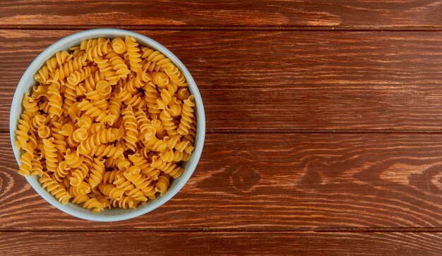 Vue de dessus des pâtes rotini dans un bol sur une surface en bois avec copie espace