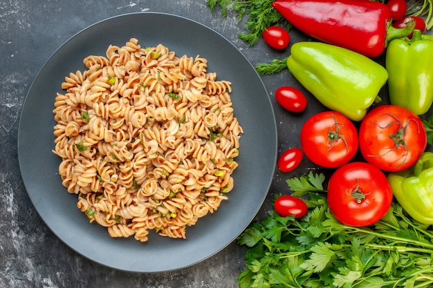 Vue de dessus des pâtes rotini sur plaque ronde poivrons tomates tomates cerises aneth persil sur tableau gris