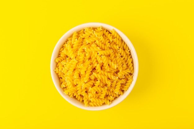 Photo gratuite une vue de dessus des pâtes sèches italiennes formées de petites pâtes crues jaunes à l'intérieur d'un bol rond de couleur crème isolé sur le fond jaune des pâtes alimentaires spaghetti italien