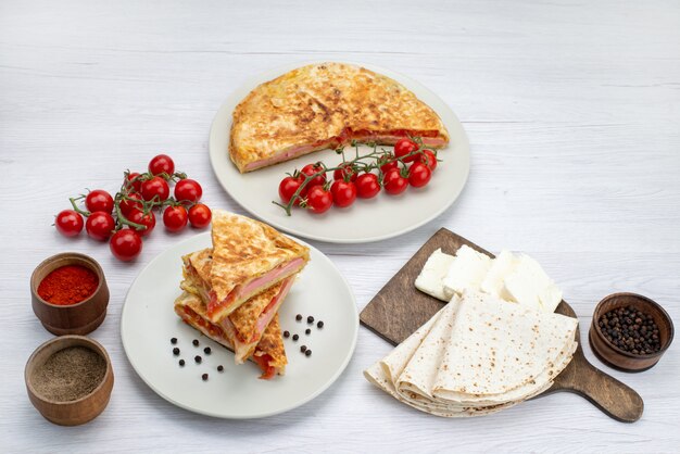 Vue de dessus de la pâtisserie de légumes cuits ronde à l'intérieur de la plaque blanche avec du fromage blanc et des tomates fond blanc repas alimentaire pâtisserie déjeuner verts