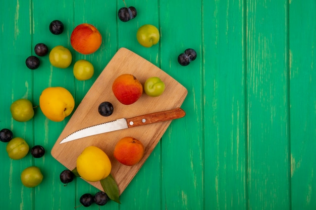 Photo gratuite vue de dessus des pêches fraîches sur une planche de cuisine en bois avec un couteau sur fond vert avec espace copie