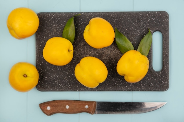 Vue de dessus des pêches jaunes fraîches sur une planche à découper de cuisine avec un couteau sur fond bleu