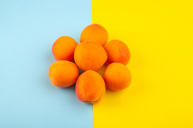 Une vue de dessus les pêches orange aigre savoureux fœtus frais bordés sur la glace-fond bleu-jaune fruits jus d'été exotique