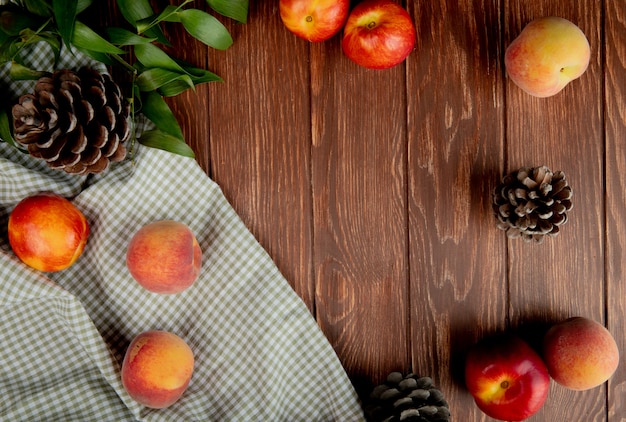 Vue de dessus des pêches et des pommes de pin sur tissu sur bois