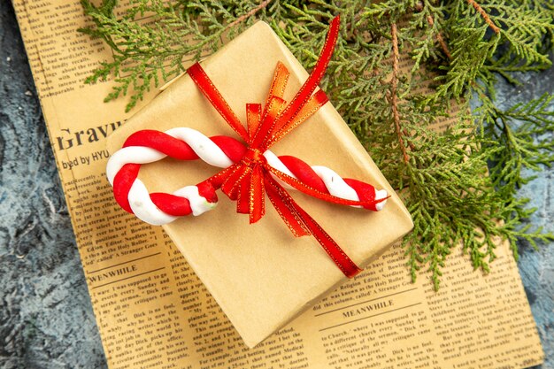 Vue de dessus petit cadeau attaché avec des bonbons de Noël ruban rouge sur des branches de pin journal sur une surface grise