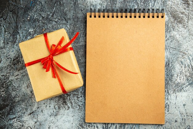 Vue de dessus petit cadeau attaché avec un cahier à ruban rouge sur une surface grise