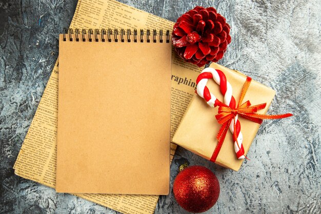 Vue de dessus petit cadeau attaché avec un carnet de ruban rouge sur des jouets d'arbre de Noël de journal sur une surface grise
