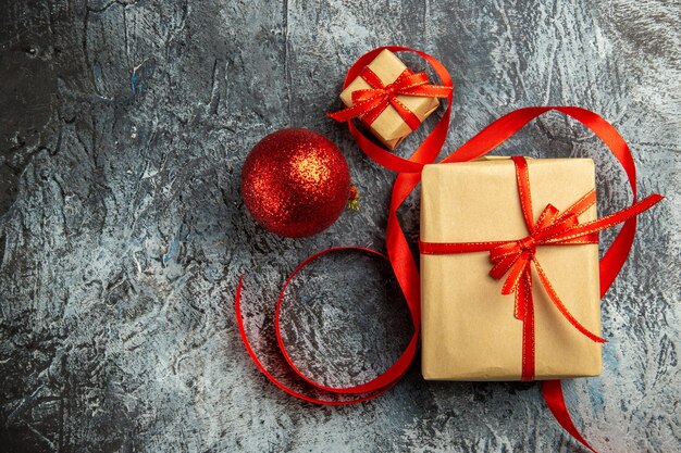 Vue de dessus petit cadeau attaché avec un ruban rouge boule de Noël rouge sur une surface sombre