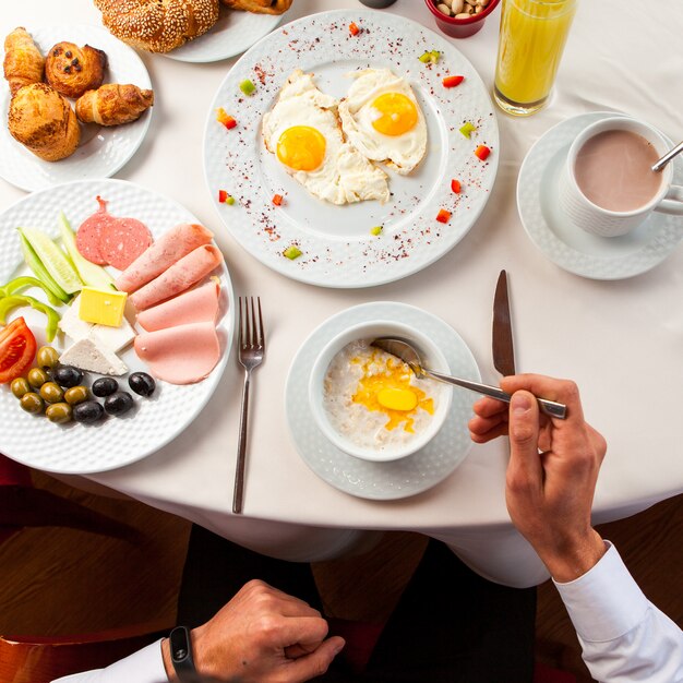 Vue de dessus petit-déjeuner assorti avec flocons d'avoine et œufs sur le plat, main humaine en plaque blanche