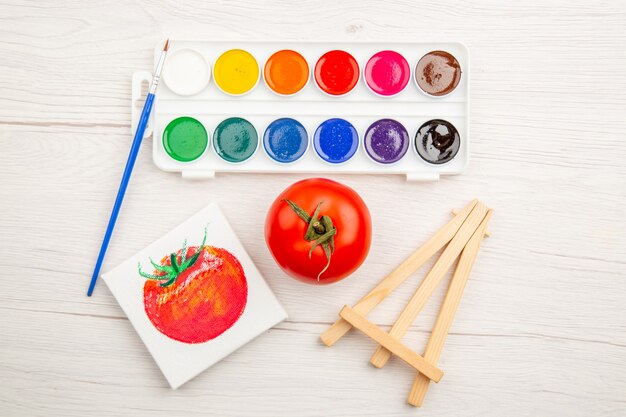 Vue de dessus petit dessin de tomate avec des peintures colorées sur tableau blanc