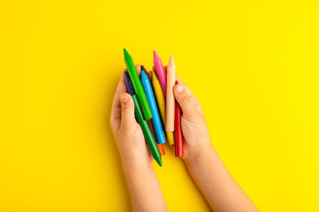 Vue de dessus petit enfant tenant des crayons colorés sur une surface jaune