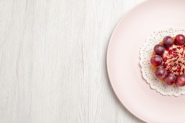 Vue de dessus petit gâteau aux raisins à l'intérieur de la plaque sur le sol blanc gâteau dessert aux fruits