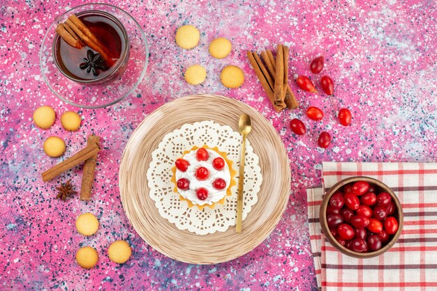 Vue de dessus petit gâteau avec de la crème fraîche et des fruits frais avec de la cannelle et du thé sur le cookie lumineux de bureau