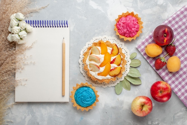 Vue de dessus petit gâteau crémeux avec des fruits tranchés et de la crème blanche avec des gâteaux et des fruits crémeux sur un sol blanc léger biscuit gâteau aux fruits sucré