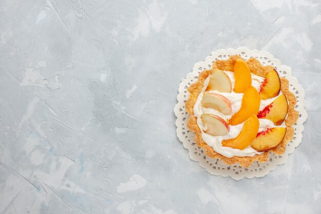 Vue de dessus petit gâteau crémeux avec des fruits tranchés dessus sur le fond blanc gâteau aux fruits biscuit sucré