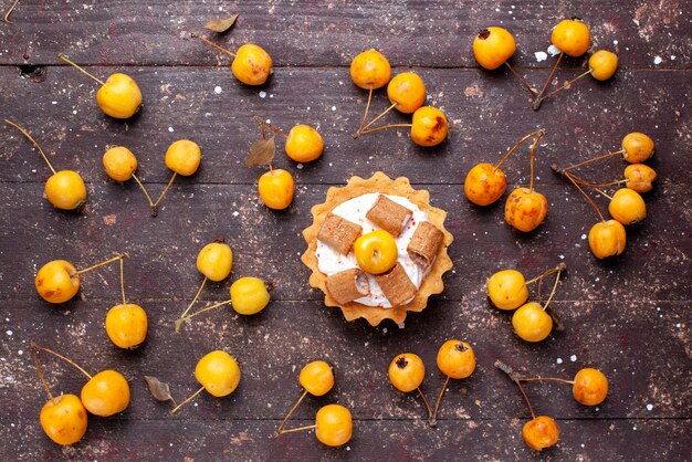 Vue de dessus petit gâteau délicieux avec des biscuits avec des cerises jaunes sur la table en bois brun fruits frais aigre moelleux mûrs