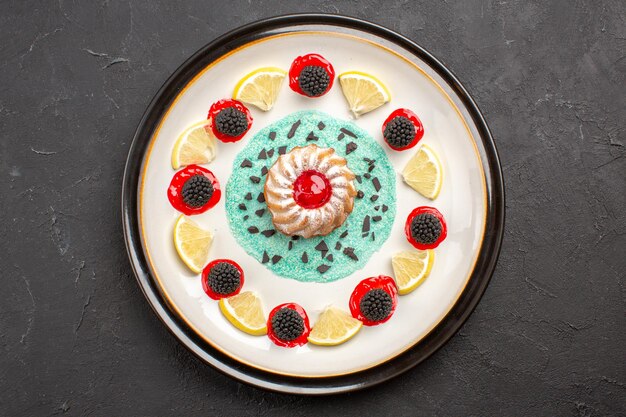 Vue de dessus petit gâteau délicieux avec confitures et tranches de citron à l'intérieur de la plaque sur fond sombre biscuit aux agrumes aux fruits biscuit sucré