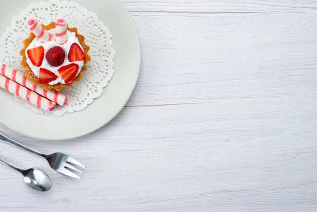 Vue de dessus petit gâteau délicieux avec de la crème et des fraises en tranches à l'intérieur de la plaque sur le fond blanc gâteau aux fruits berry sucre sucré