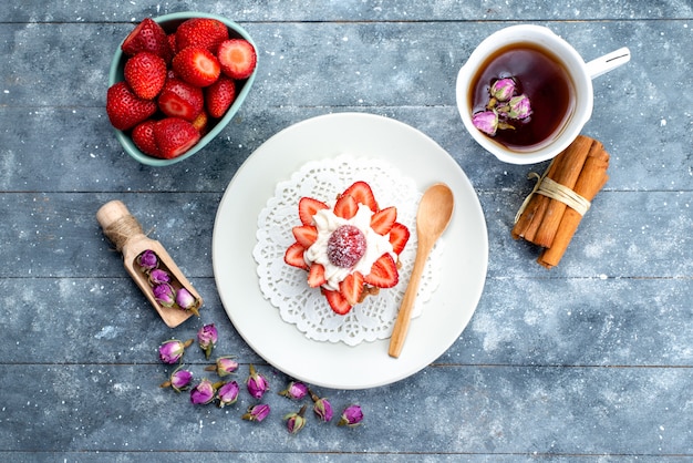 Photo gratuite une vue de dessus petit gâteau délicieux avec de la crème à l'intérieur de la plaque avec des fraises fraîches et du thé sur le fond bleu-gris cookie biscuit gâteau aux fruits