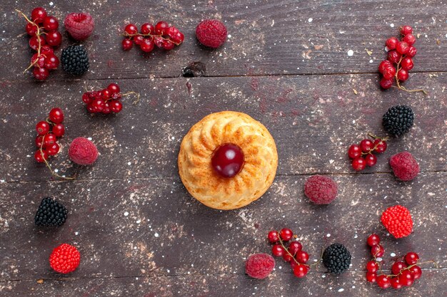 Vue de dessus petit gâteau délicieux avec différentes baies colorées réparties sur toute la table marron berry fruits couleur biscuit cuire au four