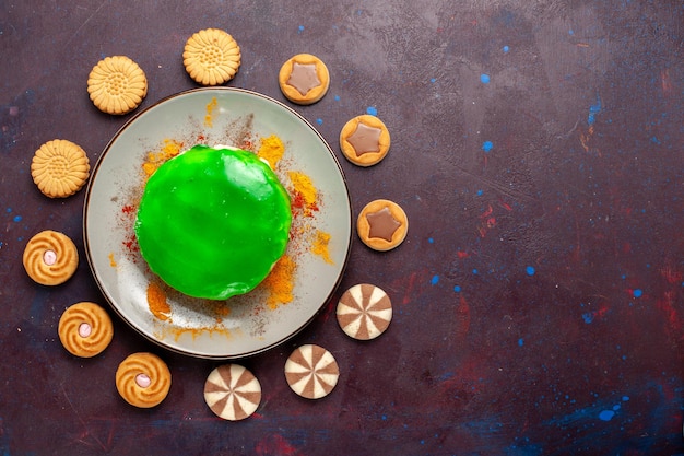 Vue de dessus petit gâteau délicieux avec différents biscuits sur la surface sombre