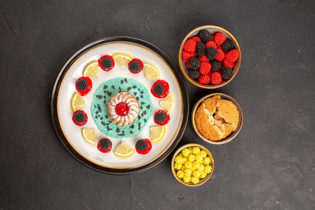 Vue de dessus petit gâteau délicieux avec des tranches de citron et des bonbons sur fond sombre gâteau aux biscuits aux agrumes aux agrumes