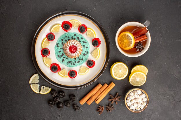 Vue de dessus petit gâteau délicieux avec des tranches de citron et une tasse de thé sur un fond sombre biscuit aux agrumes aux fruits biscuit sucré