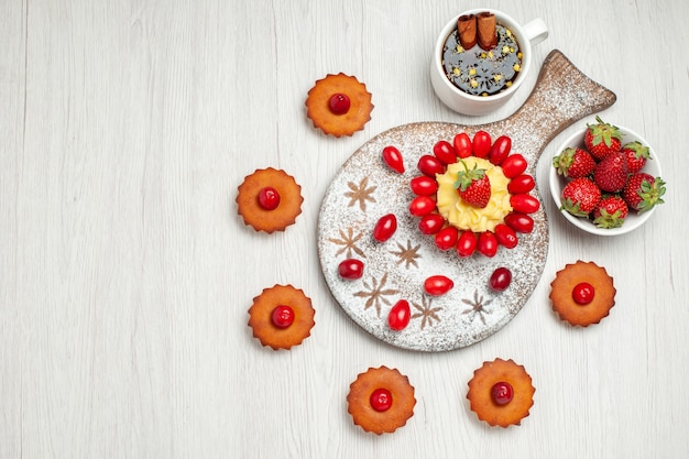 Vue de dessus petit gâteau avec du thé aux fruits et des gâteaux sur un bureau blanc