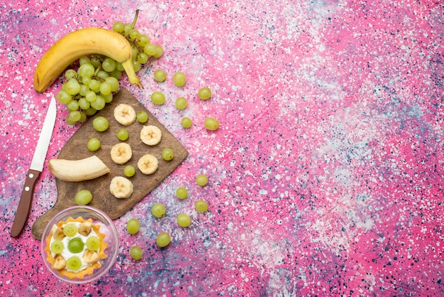 Vue de dessus petit gâteau avec des raisins frais et des bananes sur la surface violet vif gâteau aux fruits couleur douce et fraîche