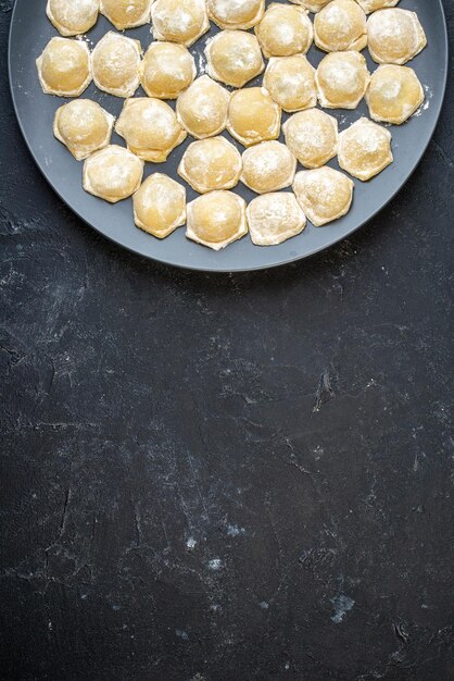 Vue de dessus petite pâte crue avec de la farine sur le fond sombre photo couleur gâteau petit pain biscuit pâte boulette tarte