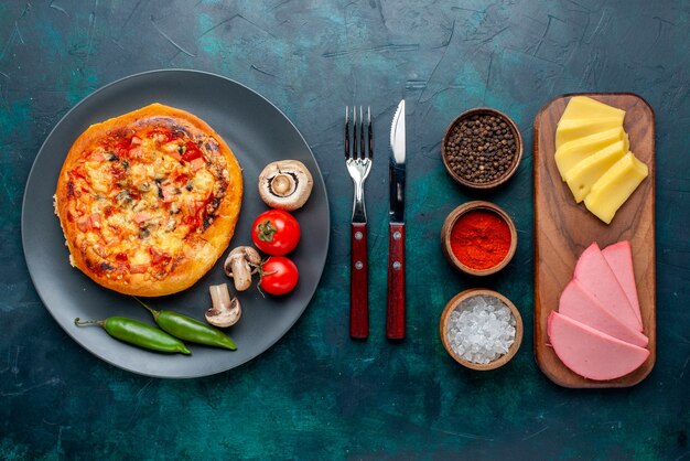 Vue de dessus de la petite pizza au fromage avec assaisonnements de légumes et de fromage sur une surface bleu foncé