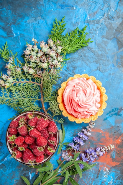 Vue de dessus de la petite tarte avec bol de crème pâtissière rose aux framboises sur surface bleue