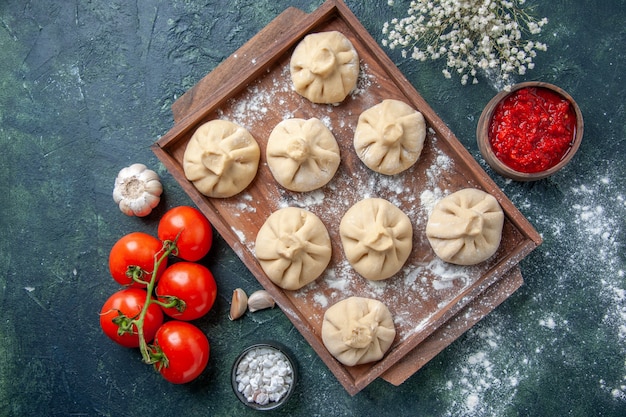 Vue de dessus de petites boulettes crues avec de la viande et des tomates sur une surface sombre repas de couleur farine plat de cuisson de la viande