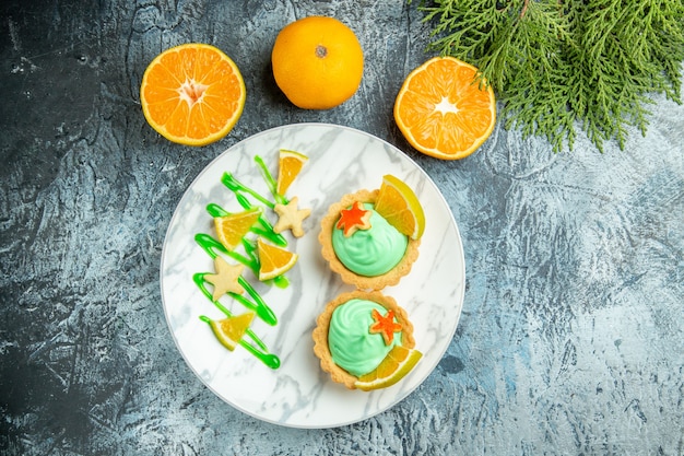 Vue de dessus de petites tartelettes à la crème pâtissière verte et tranche de citron sur le bloc-notes des oranges coupées plaque sur table sombre