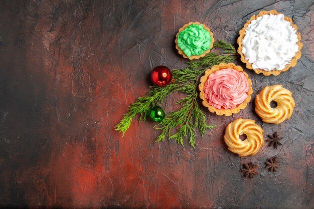 Vue de dessus de petites tartes biscuits anis étoilés arbre de Noël jouets sur une surface rouge foncé