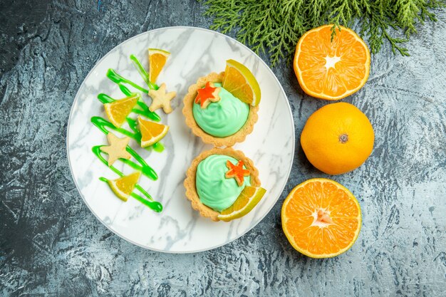 Vue de dessus de petites tartes à la crème pâtissière verte et tranche de citron sur la plaque coupées oranges sur table sombre